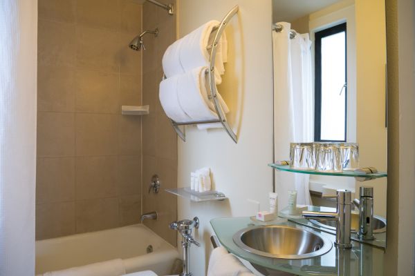 This image shows a modern bathroom with a bathtub, sink, mirror, towels, and toiletries neatly arranged. The space is well-lit with natural light.