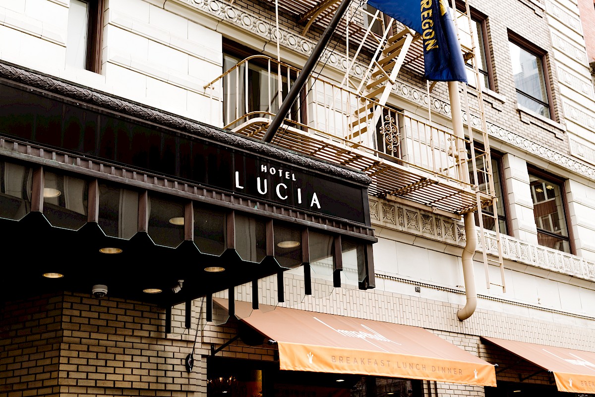 The image shows the exterior of Hotel Lucia with a sign and awnings, alongside a fire escape and building facade.
