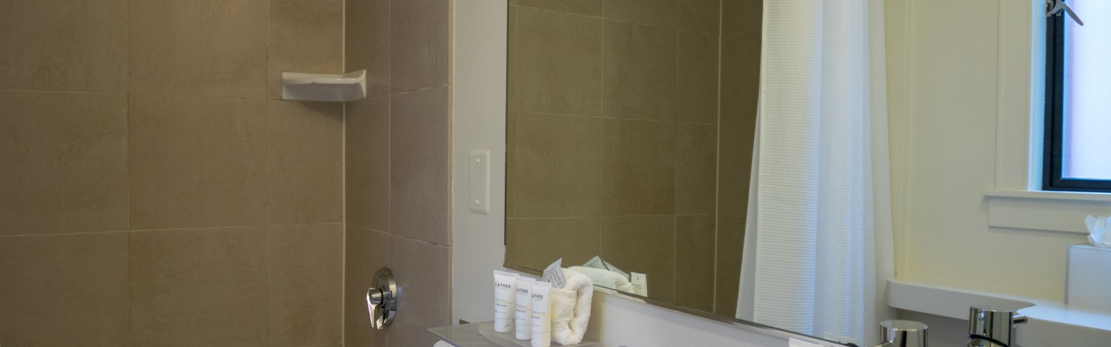 A modern bathroom features a bathtub with a shower, sink with a faucet, mirror, and toiletries neatly arranged by the sink.