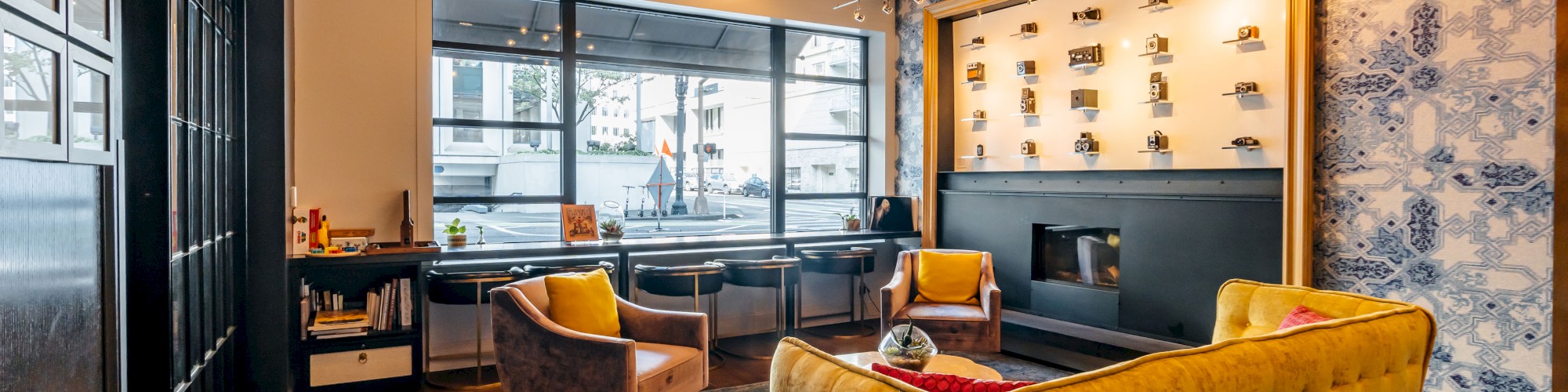 A stylish lounge with a yellow sofa, armchairs, art, shelves, large window, and modern chandelier on a cozy rug.