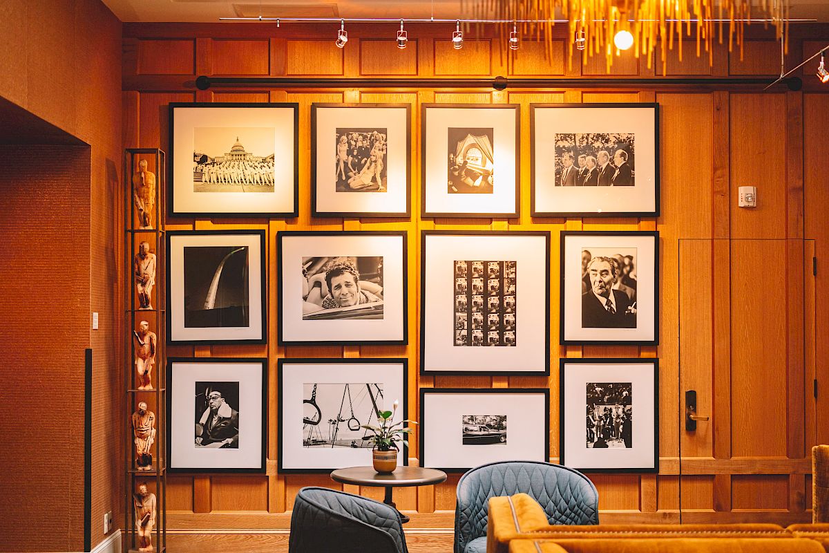 A wall decorated with framed photographs in a cozy, warmly-lit room featuring a small round table, chairs, and wood-paneled walls ends the sentence.