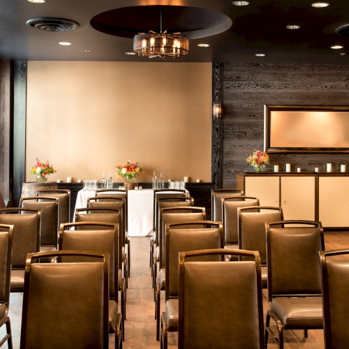 The image shows a small conference room with rows of chairs facing a table, decorated with flowers and candles, and a modern aesthetic.