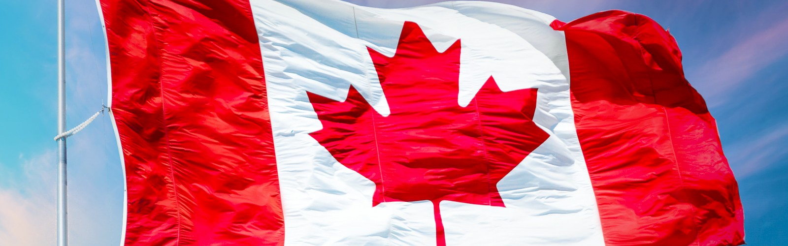 This image shows the national flag of Canada waving against a bright sky, featuring a red maple leaf in the center with red and white color blocks.