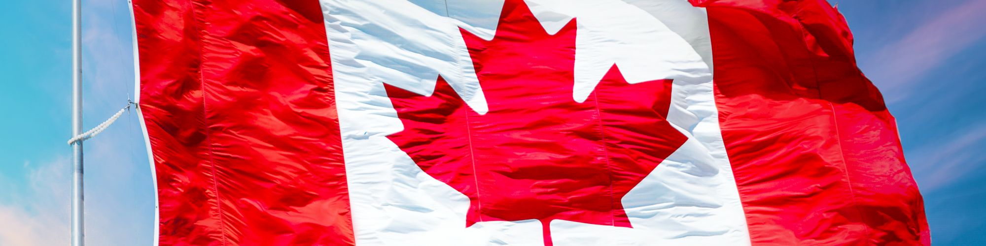 This image shows the national flag of Canada waving against a bright sky, featuring a red maple leaf in the center with red and white color blocks.