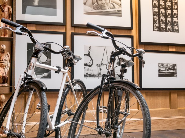 Two bicycles are parked in front of a wall adorned with black-and-white framed photos and art pieces, ending the sentence.