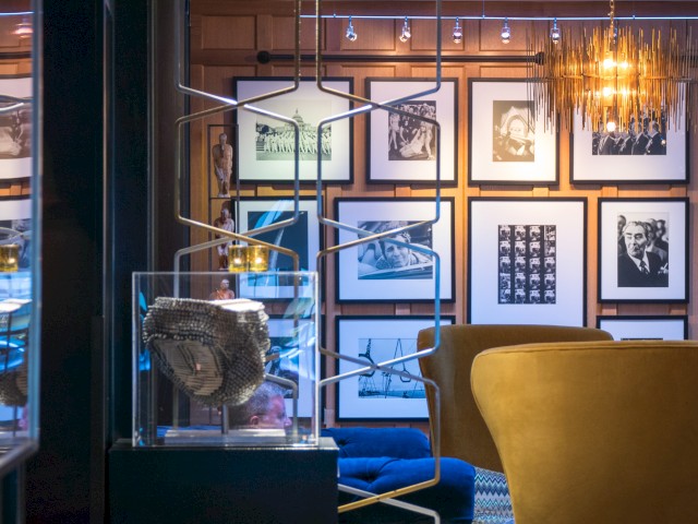 A modern interior space featuring yellow chairs, framed photos on the wall, and a unique sculpture in a glass case.