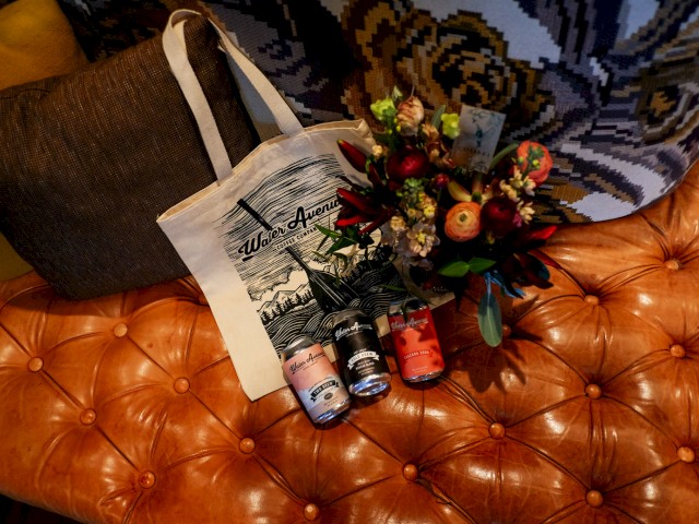 The image shows a tote bag, a bouquet of flowers, and three beverage cans placed on a tufted leather seat, all ending the sentence.