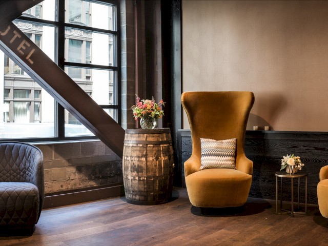 A cozy hotel lobby features two mustard-yellow high-back chairs, a dark barrel table with flowers, and an industrial decor theme, ending the sentence.