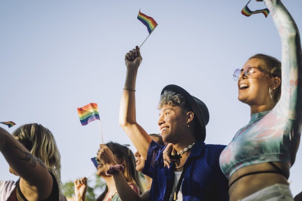 A group of people is joyfully waving rainbow flags outdoors at a celebration event.