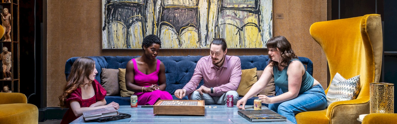 Four people sitting around a coffee table in a stylish room, with a large modern painting on the wall behind them.