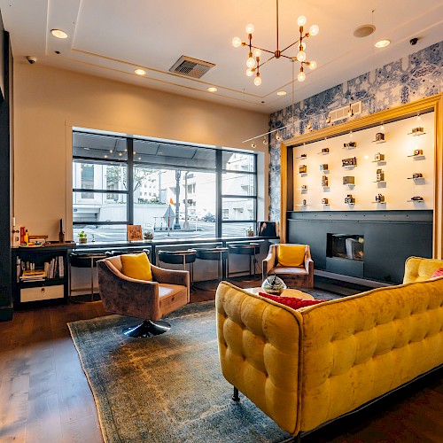 A stylish lounge with a yellow sofa, two chairs, large window, decorative wall with framed photos, and modern chandelier.