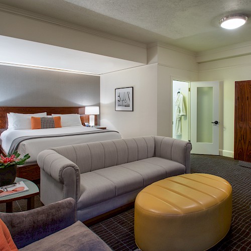 Junior Suite - A modern hotel room with a king-size bed, sofa, ottoman, desk, two nightstands, and a small table with a plant. Cozy and inviting space.