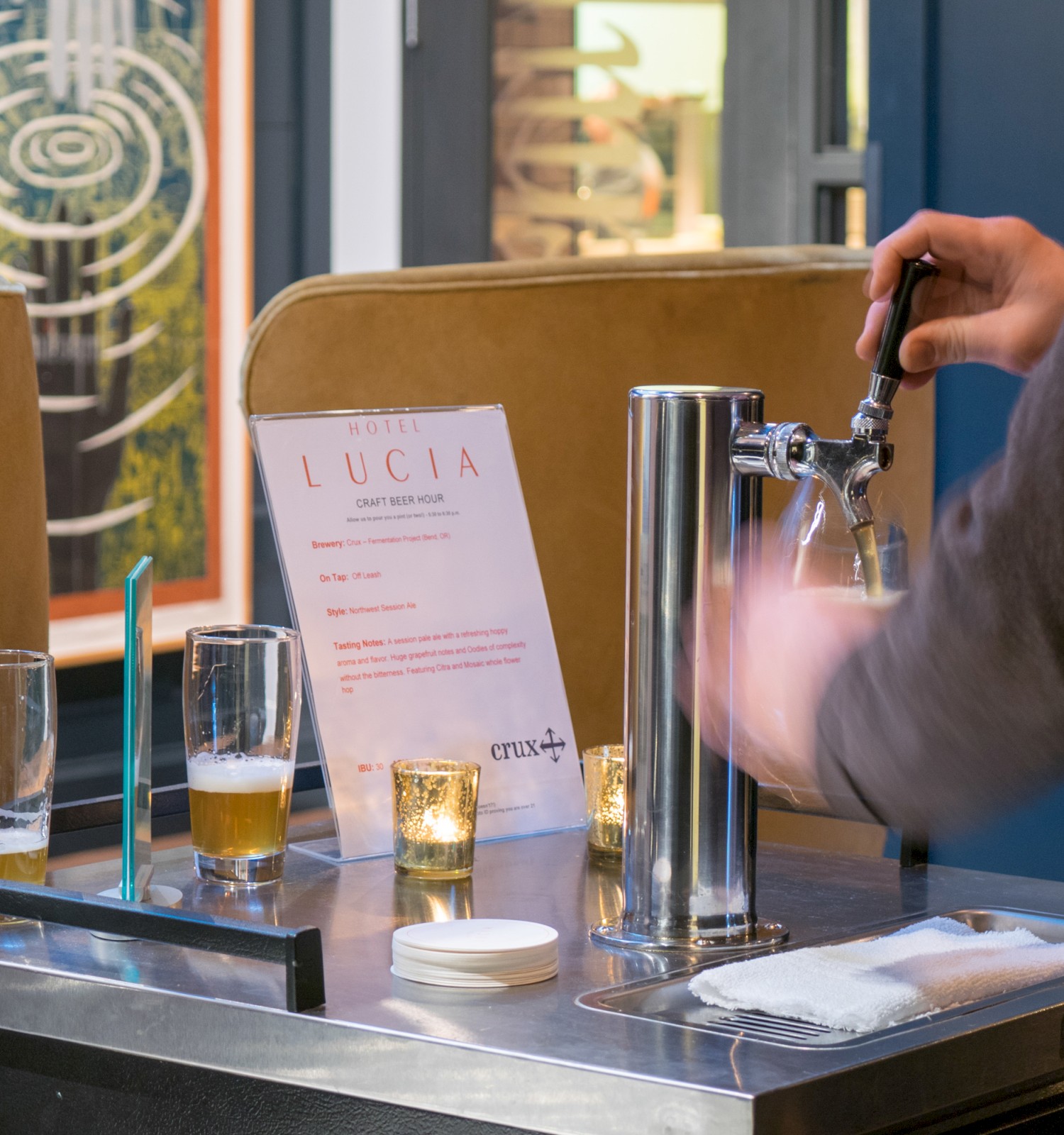 A person is pouring a drink from a tap into a glass at a bar setup with menus and candles on the counter.