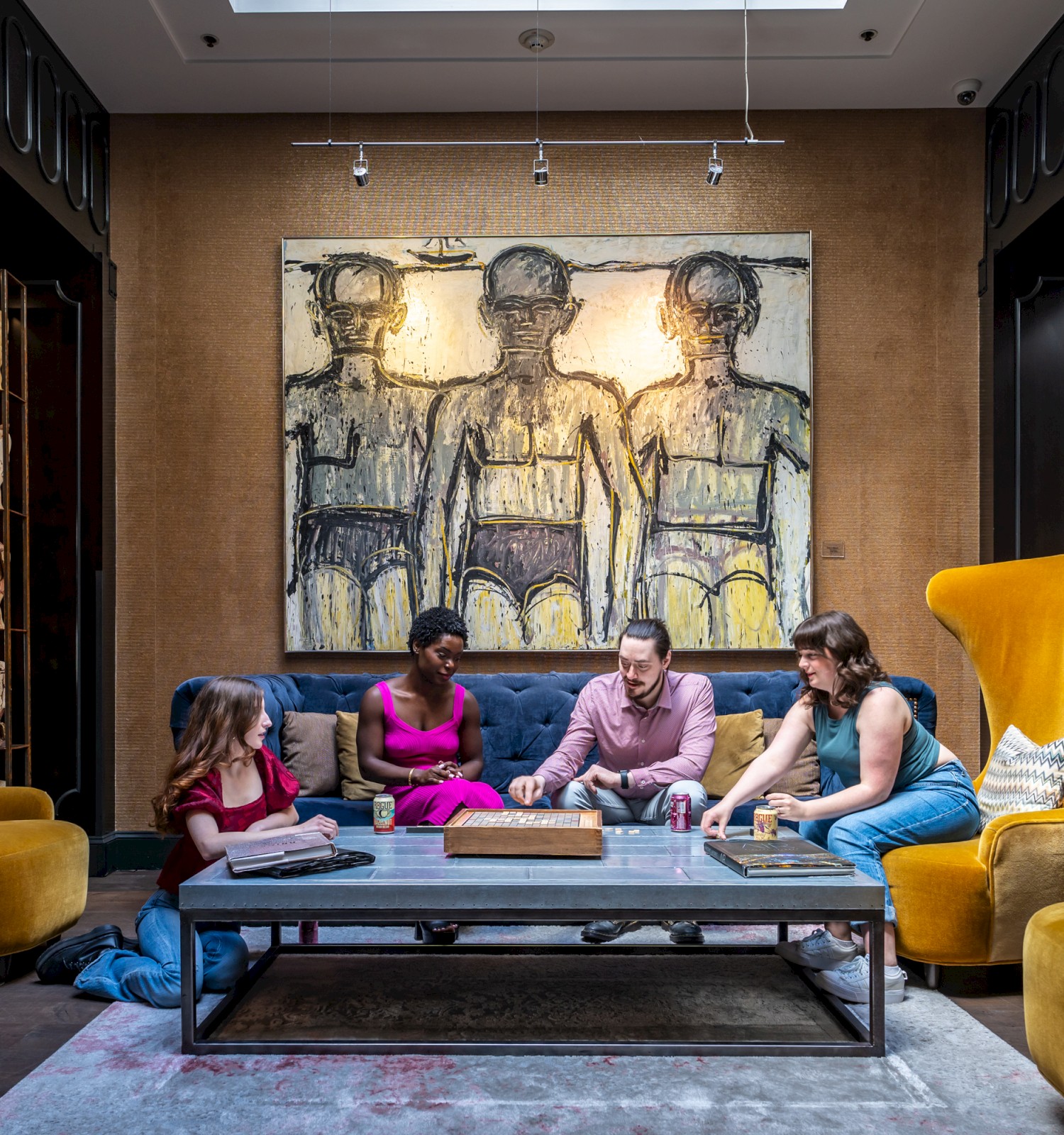 Four people sitting around a coffee table in a room with yellow chairs, paintings, and decorative items.