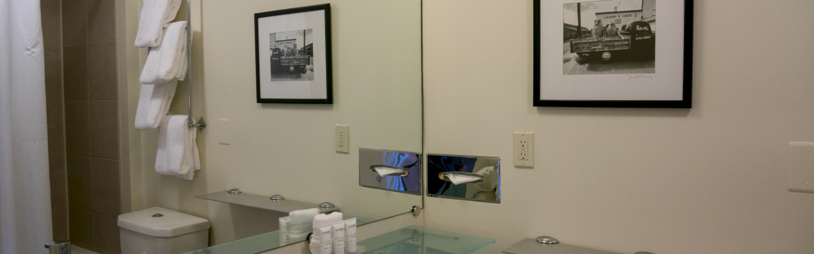 The image shows a modern bathroom with a sink, mirror, framed photo, towels, and toiletries neatly arranged.