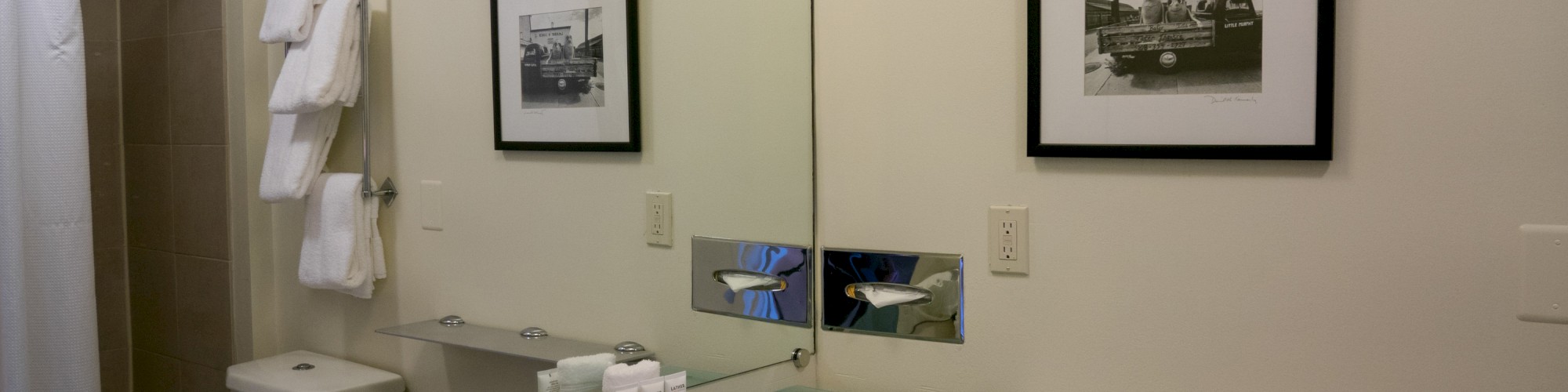 The image shows a modern bathroom with a sink, mirror, framed photo, towels, and toiletries neatly arranged.