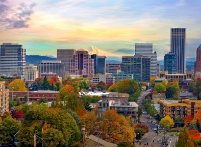 A vibrant cityscape with a mix of modern buildings and colorful autumn trees, against the backdrop of a distant snow-capped mountain.