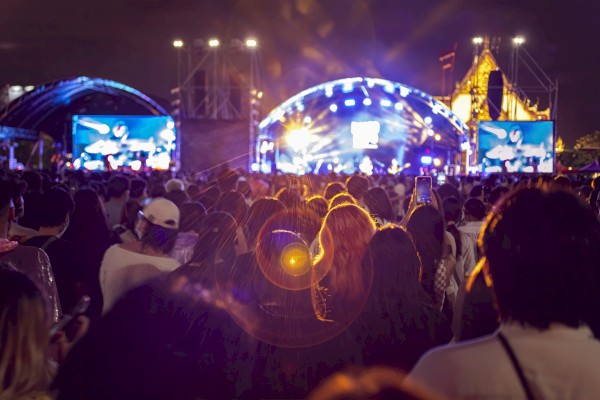 A large crowd is gathered at an outdoor concert with lit-up stages and screens displaying performers at night.