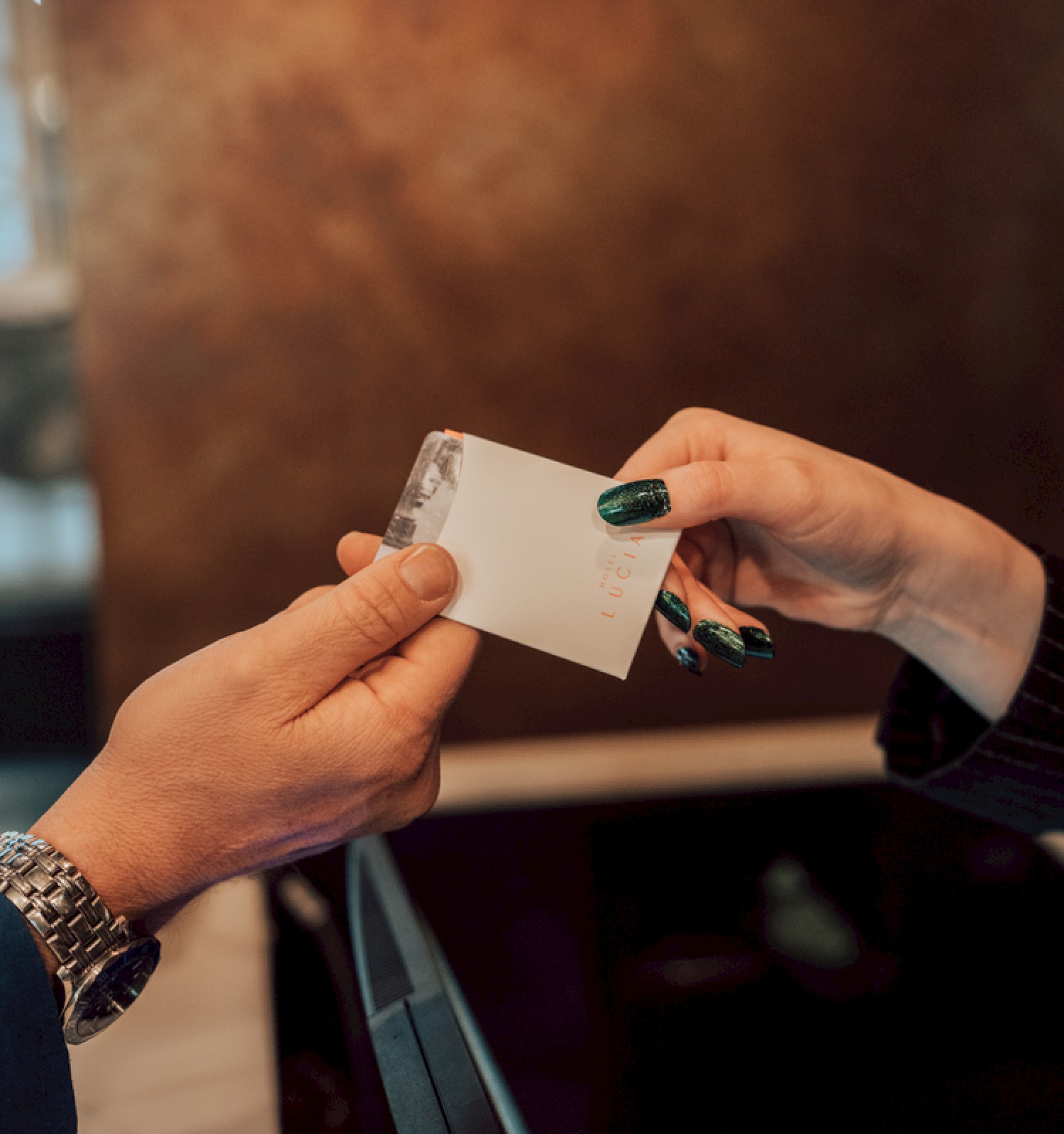 Two hands are exchanging a white card, possibly a room key or business card, in a warm indoor setting.