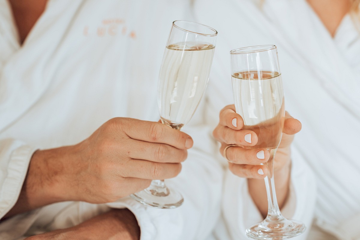 Two people in white robes clinking champagne glasses, smiling at each other.
