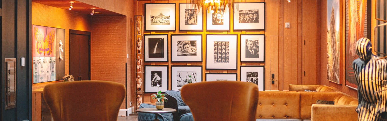 This is an image of a cozy, well-decorated art gallery lounge with framed photos on the wall, stylish chairs, and warm lighting.
