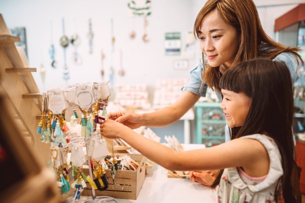 A woman and a child are selecting keychains at a store, with both smiling and engaged in the activity.