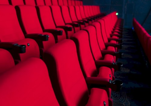 Rows of empty red theater seats in a dark auditorium setting, suggesting a cinema or performance venue.