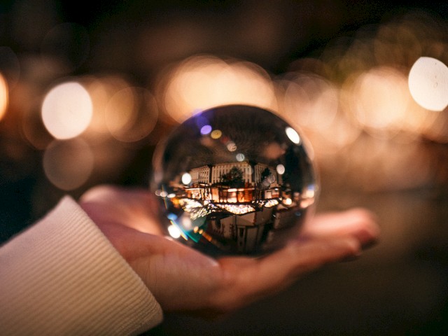 A crystal ball resting on a hand, reflecting a city street scene with warm bokeh lights in the background.