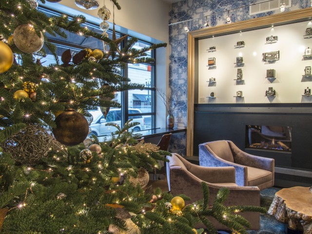 A cozy, festively decorated lobby with a large Christmas tree, seating area, and a display wall of trophies or ornaments, bright windows in the background.