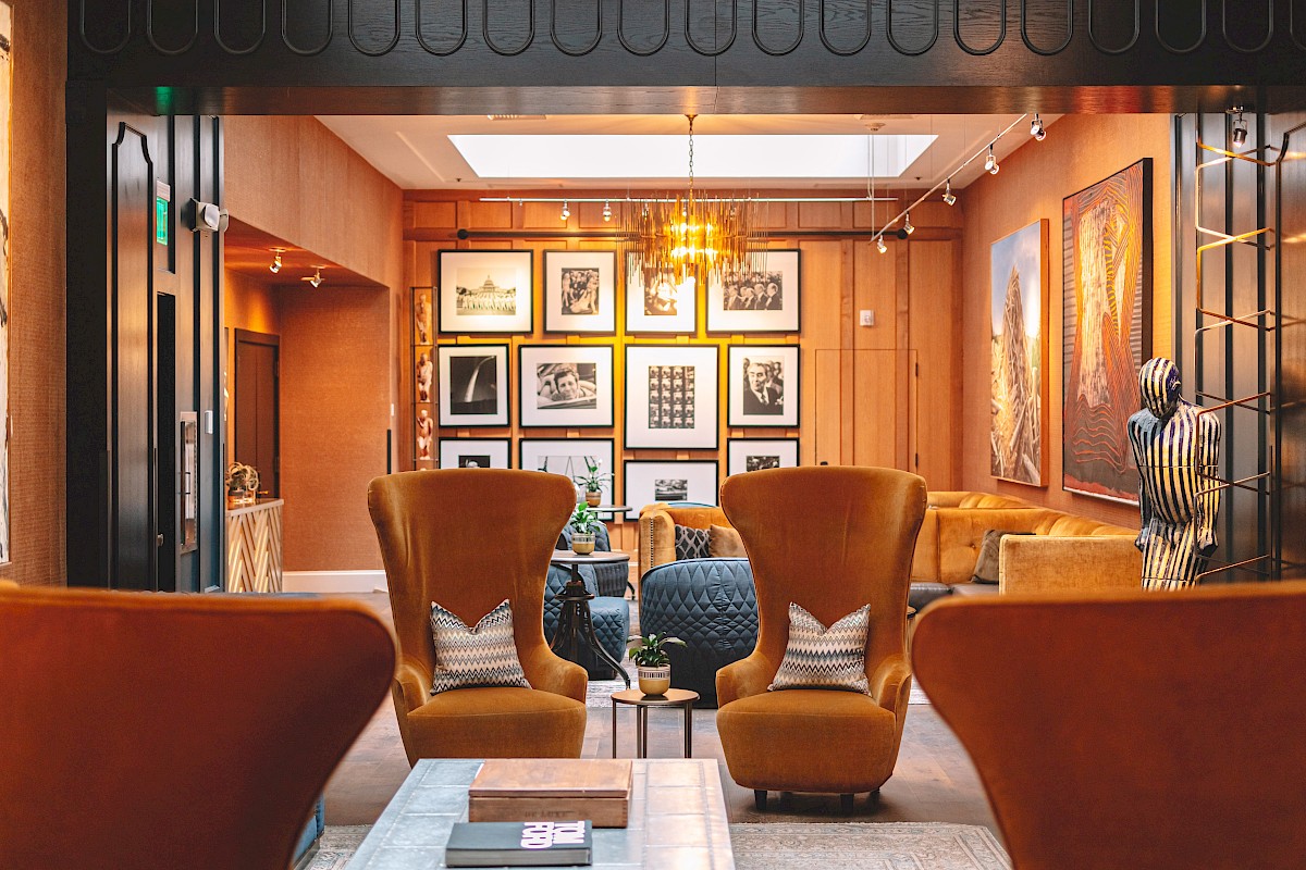 A stylish, cozy lounge with mustard chairs, black and white art on the wall, a chandelier, and warm lighting.