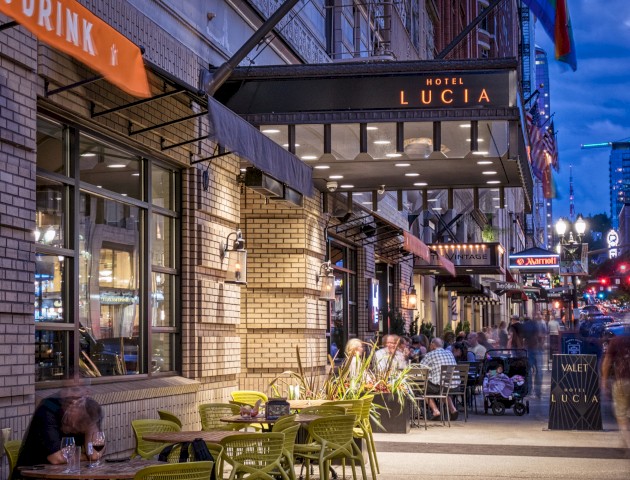 Outdoor dining scene in front of Hotel Lucia during evening, with people enjoying drinks and conversation on a lively city street.