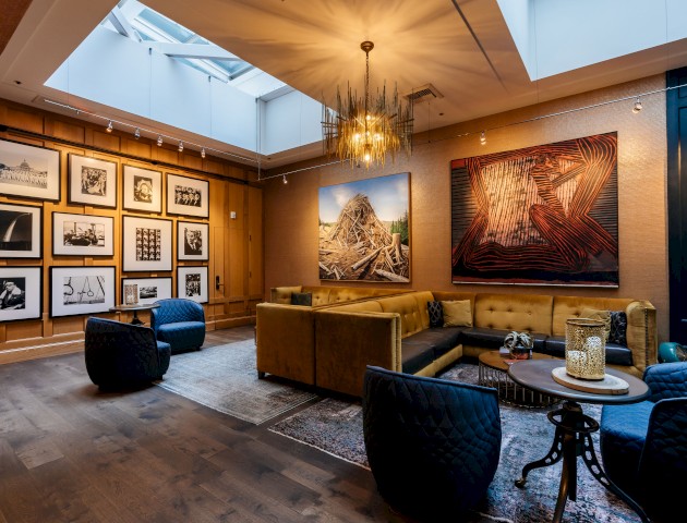 A stylish, cozy lounge with vibrant artwork, a mix of modern and vintage furniture, and a skylight providing natural light.