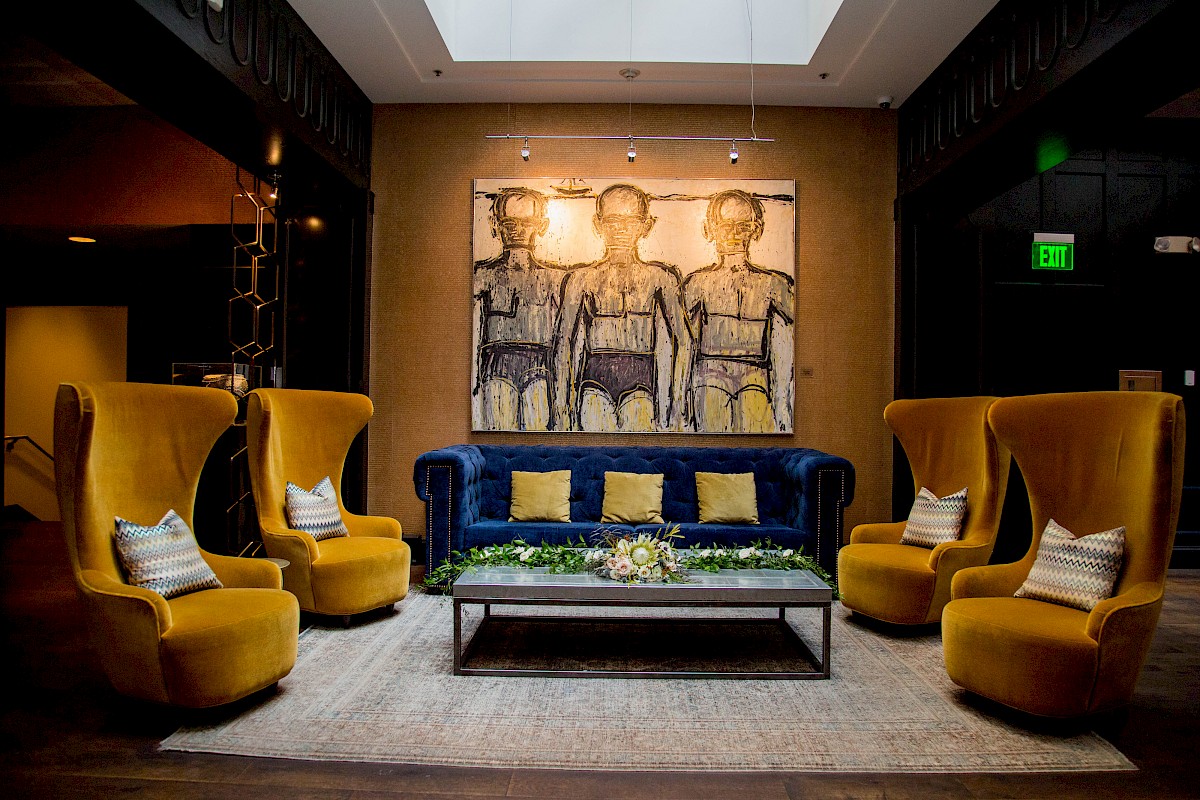 A stylish hotel lobby with a blue sofa, four yellow armchairs, a modern art painting, and cozy decor.