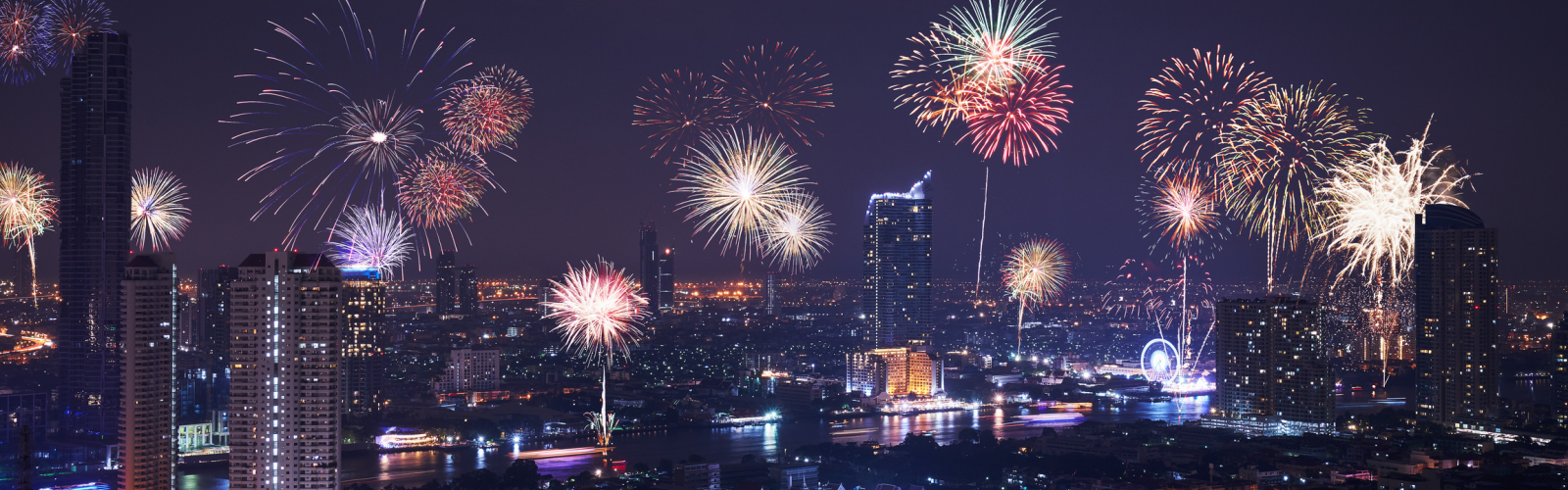 Fireworks explode over a city skyline at night, illuminating the sky with vibrant colors and patterns.