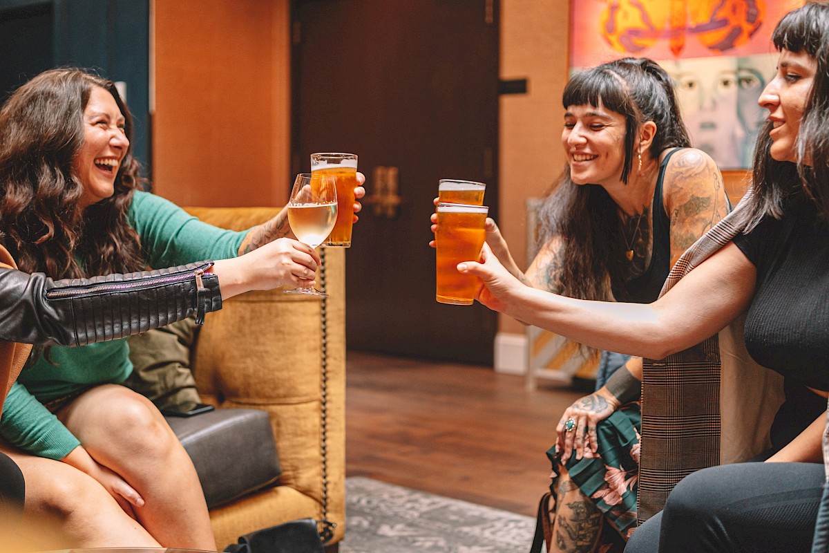 Four women are enjoying drinks and laughter together in a cozy indoor setting, celebrating friendship and good times.