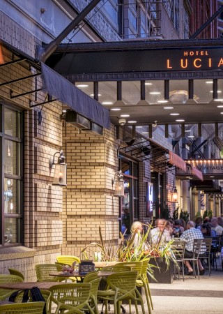 This is an outdoor dining scene at Hotel Lucia, with people enjoying a lively evening on a city street.