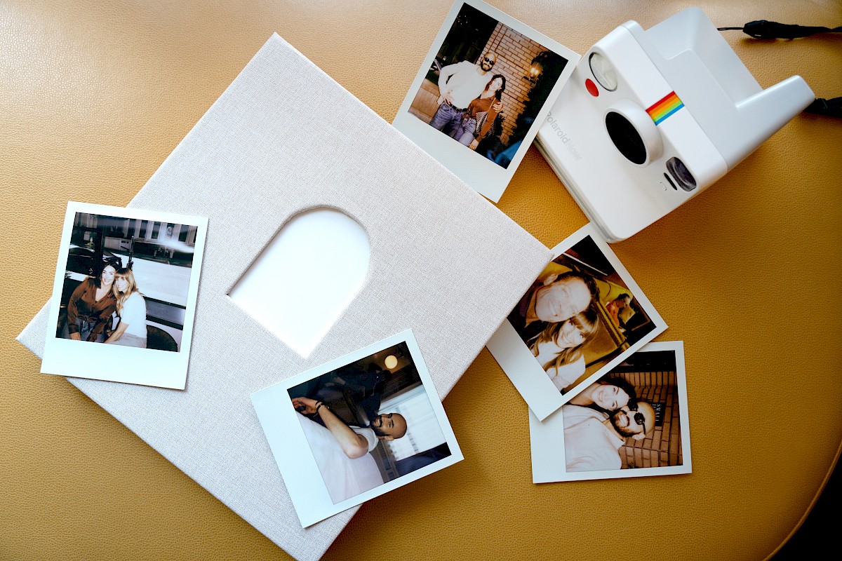 A collection of instant photos, a white photo album with an arched cutout, and a Polaroid camera on a yellow surface.