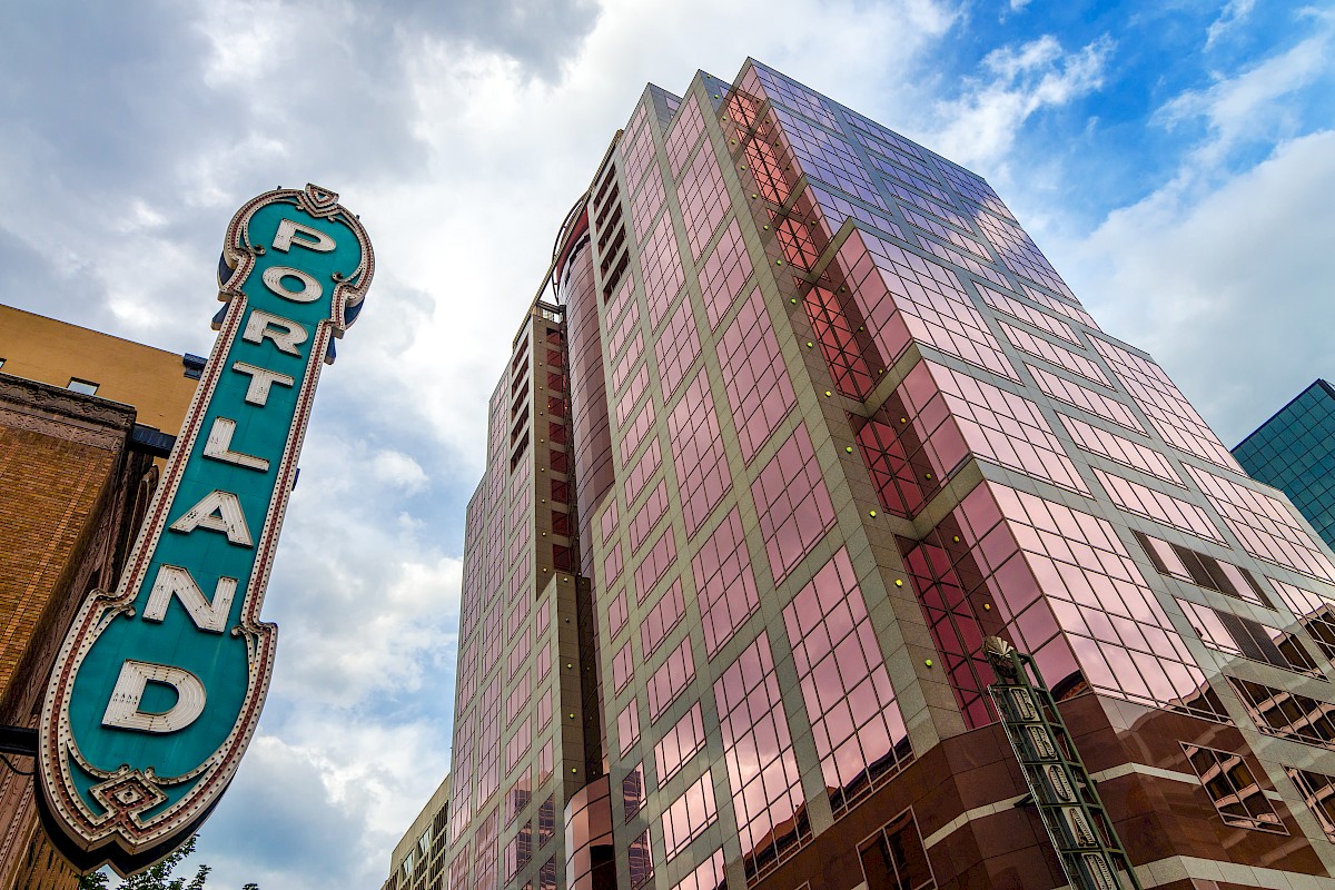 A colorful glass skyscraper with a turquoise neon sign that reads 