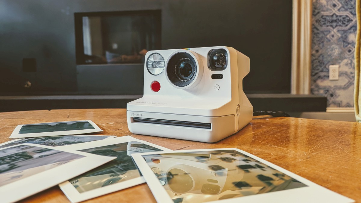 A vintage Polaroid camera placed on a wooden table, with several printed instant photographs scattered around it.