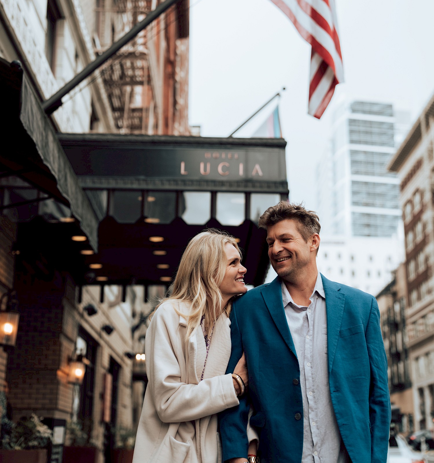 A happy couple walking and smiling on a city street near a hotel called 
